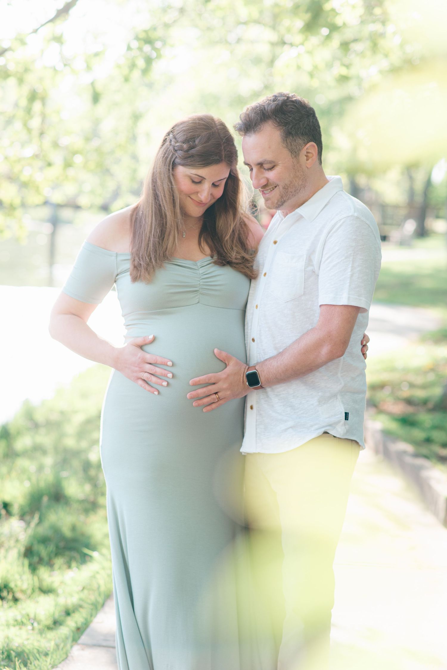 Artistic image of couple looking down at maternity belly in front of a lake at Divine park.