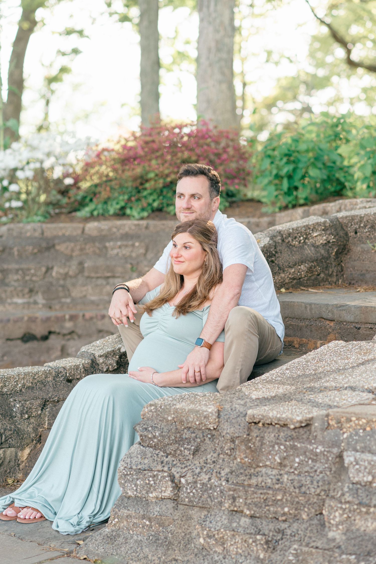 Maternity photo of expecting mother and father sitting in front of a tranquil lake at dusk, showcasing their love at a park in NJ.