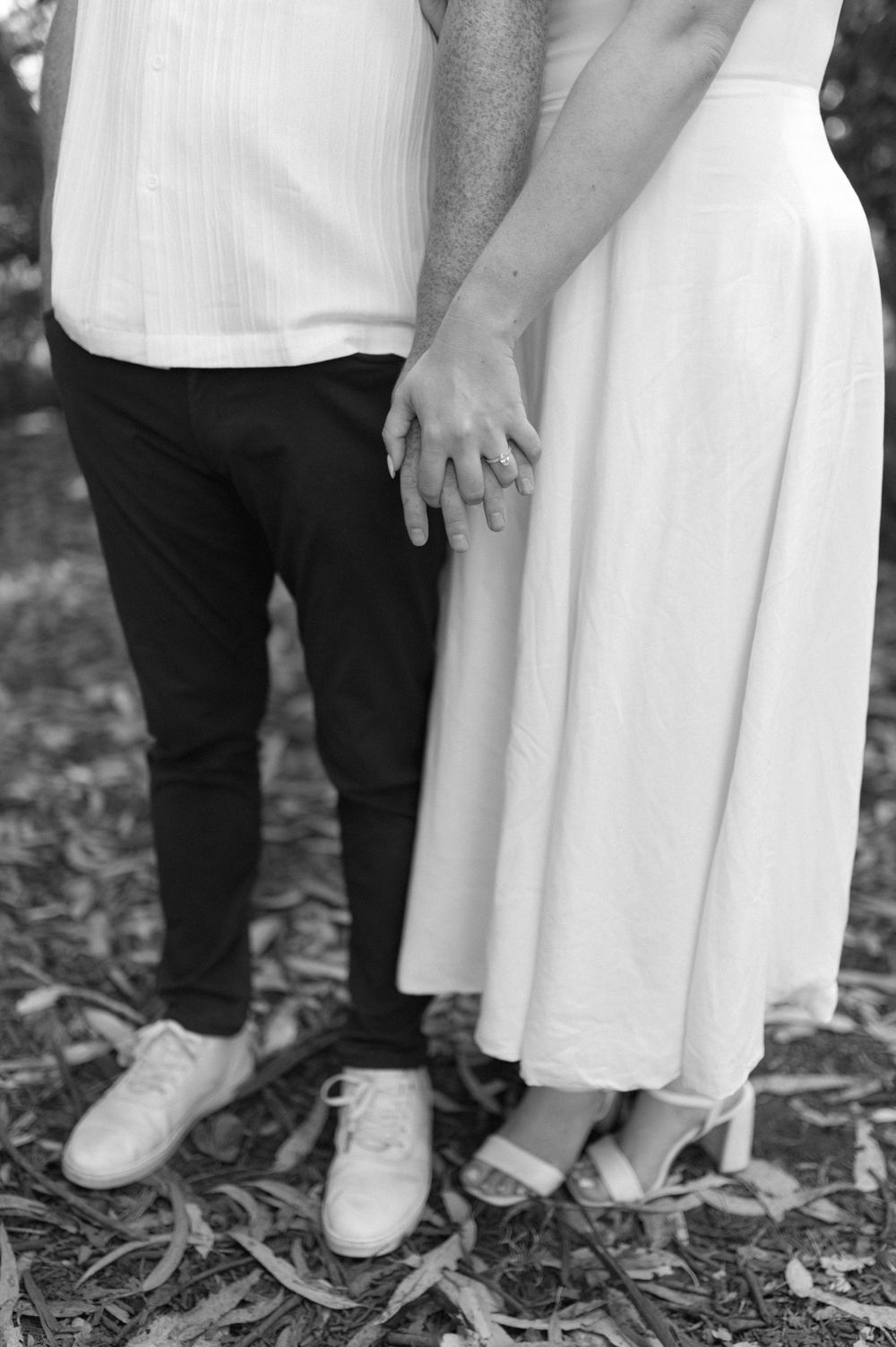 Intimate black and white photo focusing on a couple's feet and joined hands.
