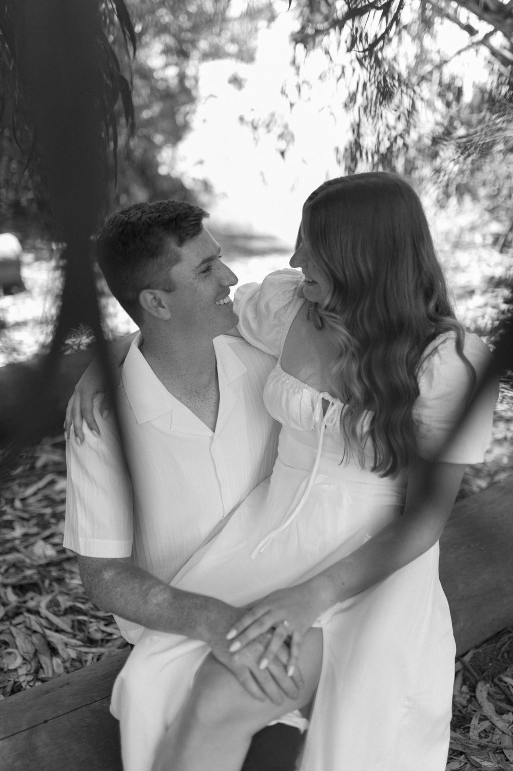 Black and white intimate portrait of a couple in white clothing sharing a tender moment outdoors.