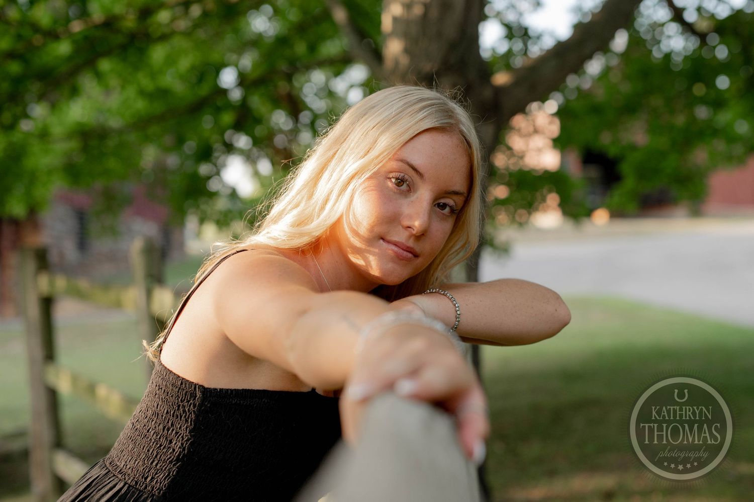 A woman rests her arms on a wooden railing in a natural outdoor setting during golden hour.