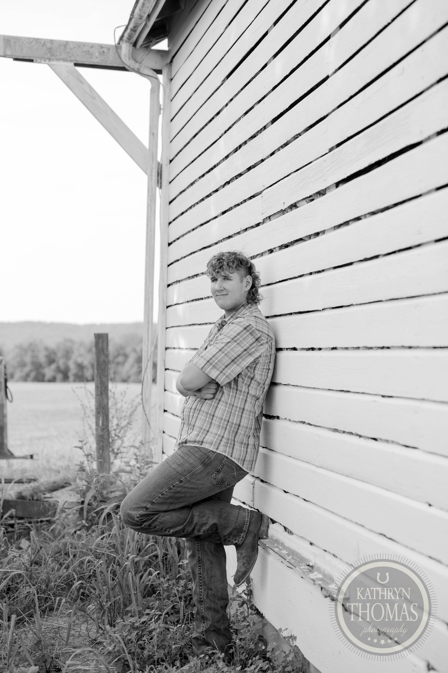 A black and white portrait of someone leaning against weathered barn siding in rural setting.