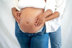 Maternity photo highlighting pregnant belly in casual jeans and white top.