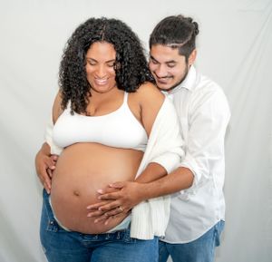 Joyful maternity photo with couple in white and denim cradling baby bump.
