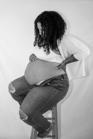 Black and white maternity photo showing pregnant woman in ripped jeans looking down at her belly.