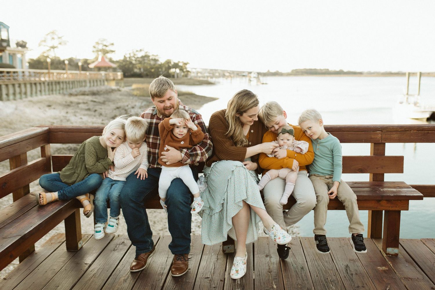 A family sits together on a wooden pier overlooking the serene May River in Bluffton, SC at sunset for a photoshoot with B. Logsdon.