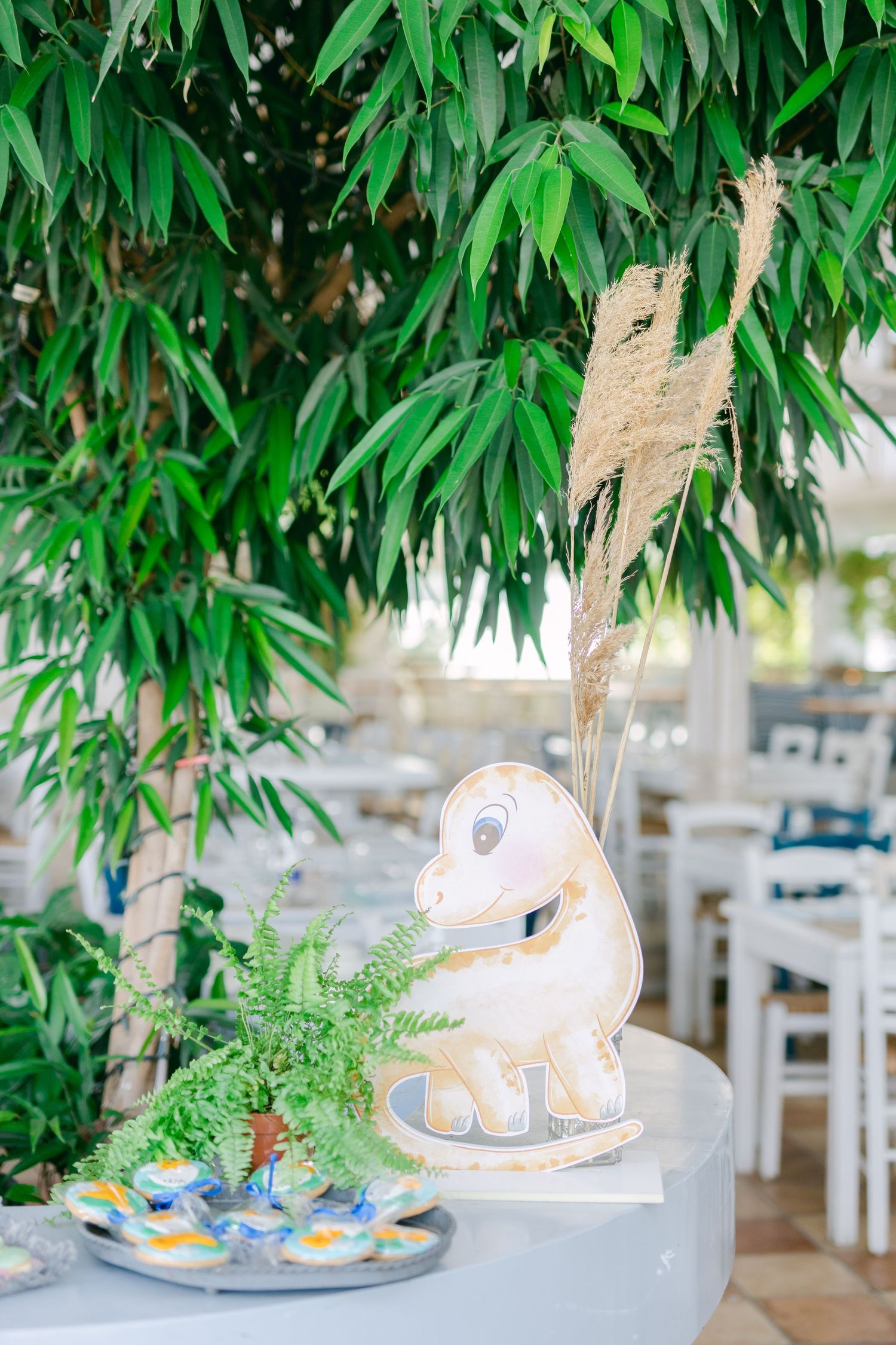 White dinosaur ornament with pampas grass and tropical greenery on a wedding table setting.