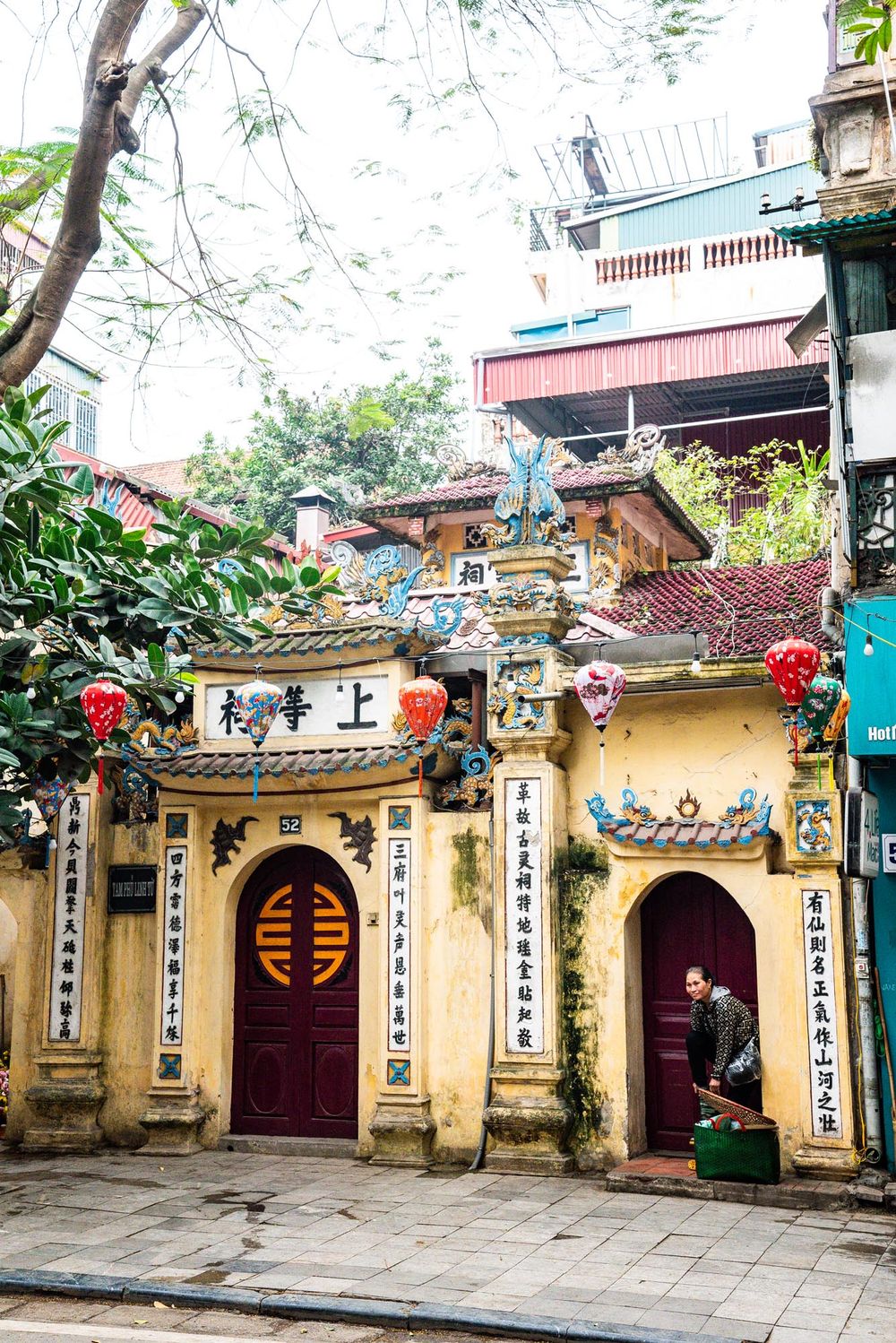 Traditional Vietnamese temple entrance with red lanterns and ornate yellow walls featuring decorative Chinese characters in Hanoi.