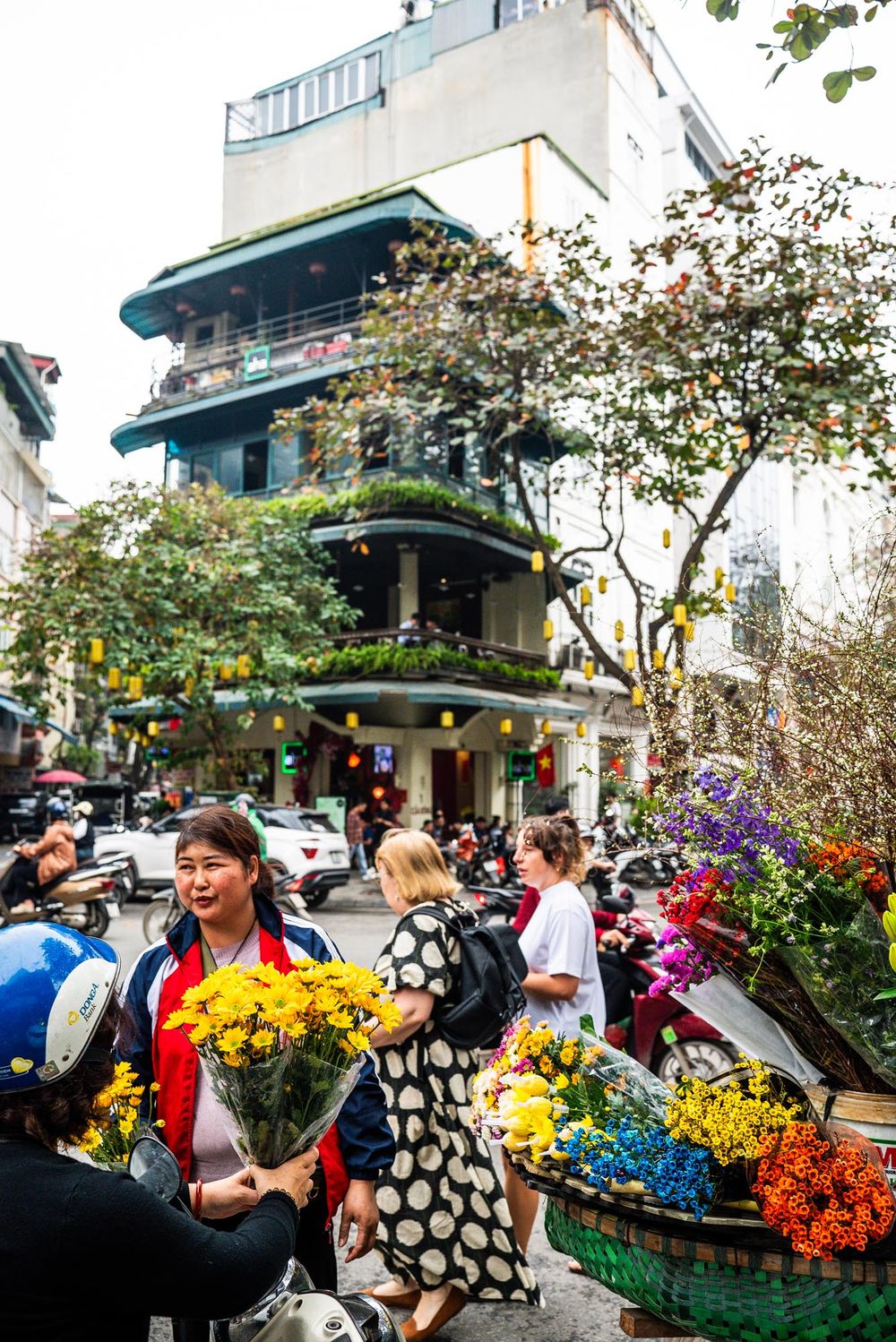 Vibrant flower market scene in Hanoi with colorful bouquets and historic colonial architecture in the background.