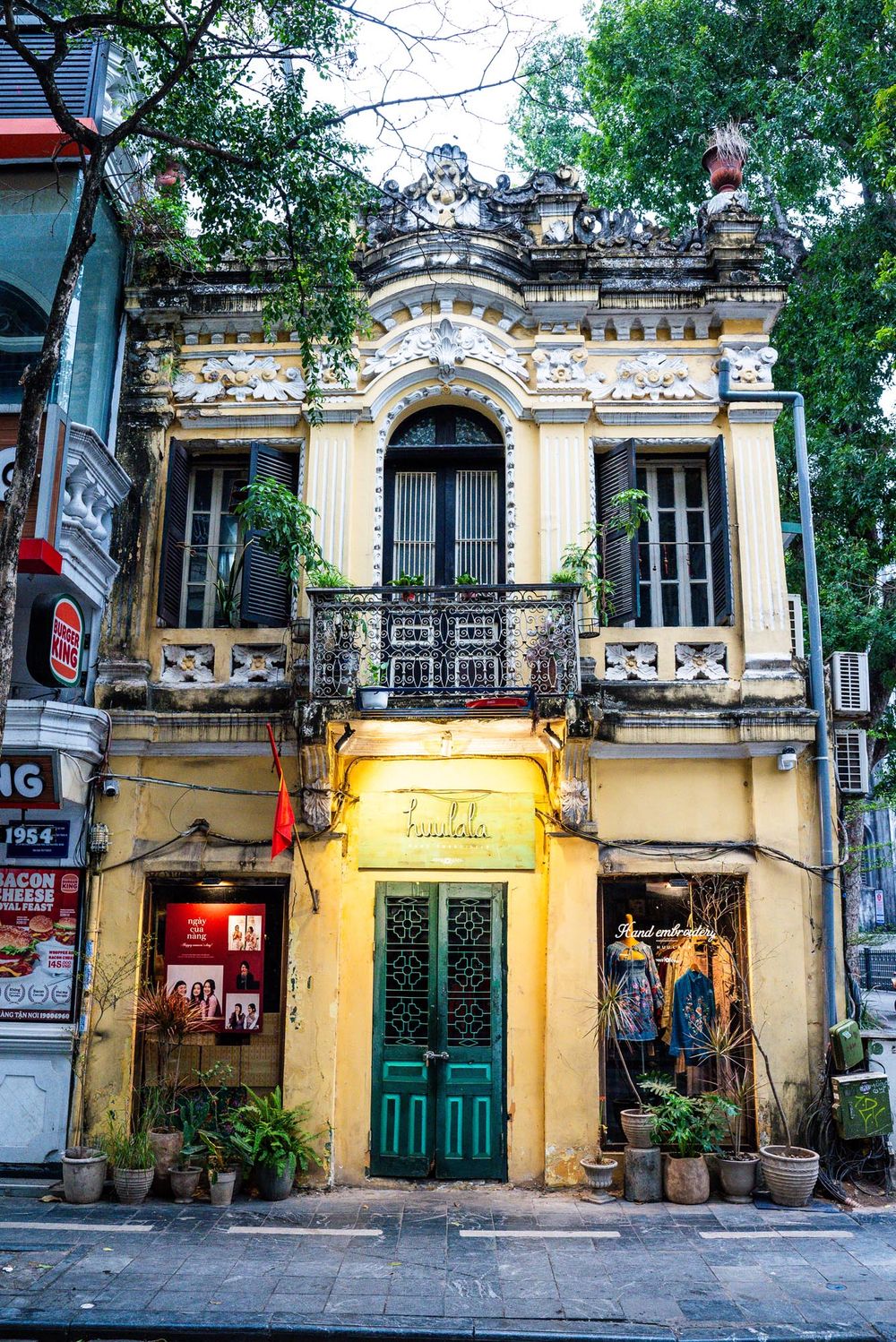 Colonial French architecture on a Hanoi street with turquoise door and ornate facade glowing in warm light at dusk.