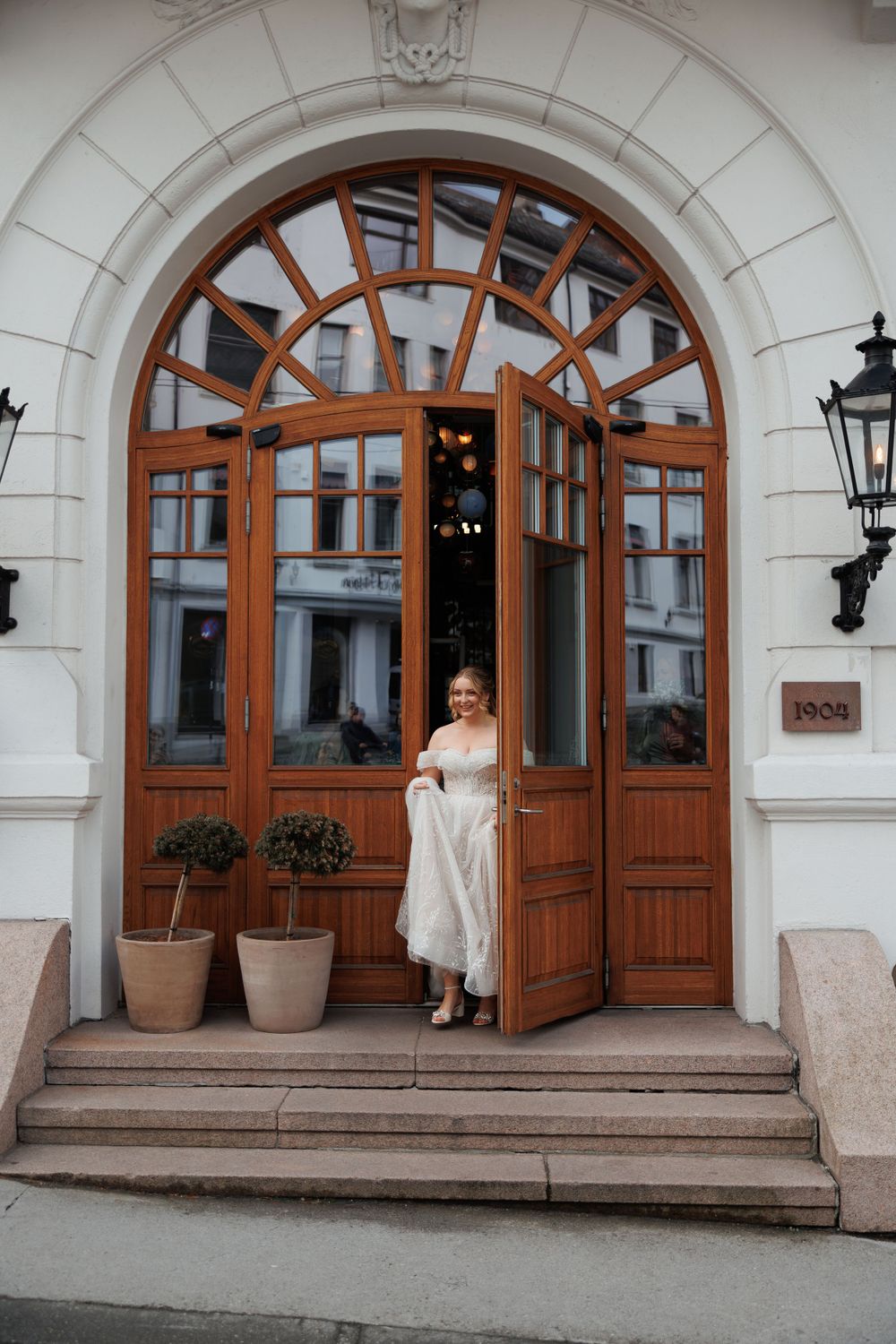 Elegant wooden arched doorway with decorative glass panels and lanterns on a white stone building entrance with steps.