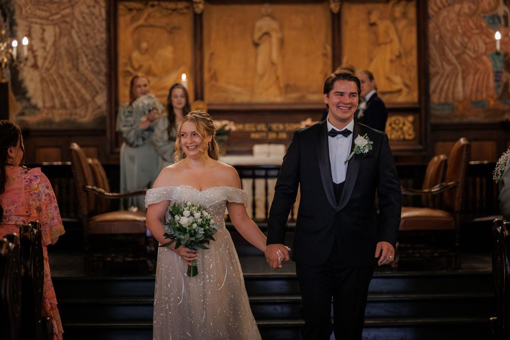 Joyful newlyweds walk down church aisle together after ceremony with beautiful altar and decorative panels in background.