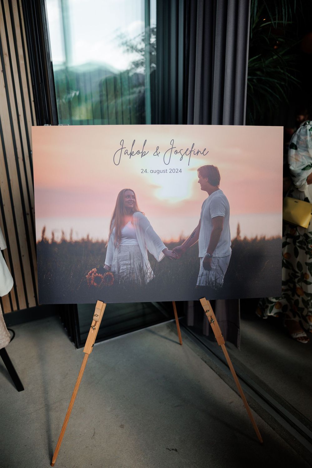 A wedding photo displayed on a wooden easel with a romantic sunset silhouette showing a couple holding hands against warm lighting.