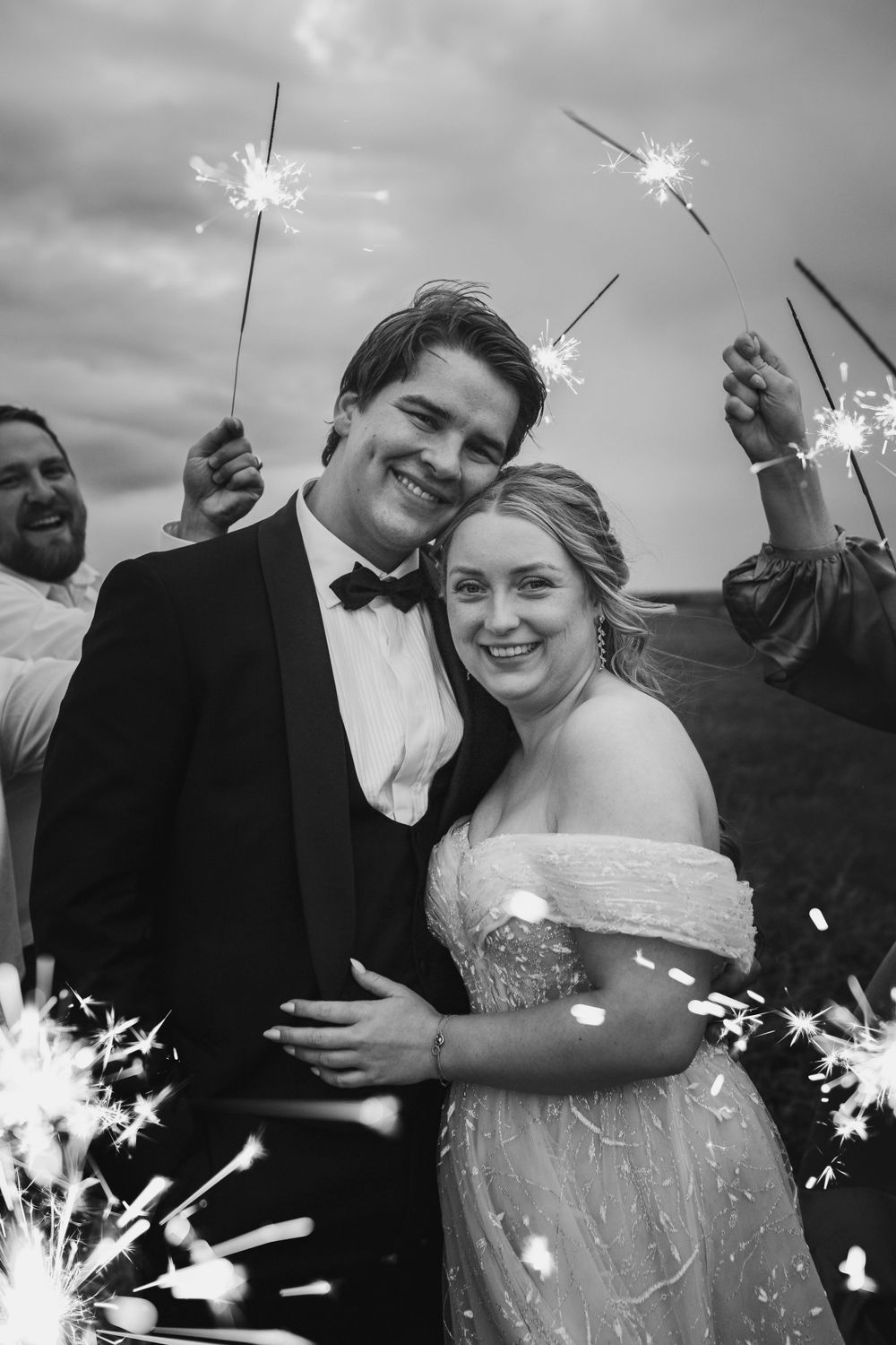 A black and white wedding celebration photo with sparklers creating a magical glowing effect around the couple.