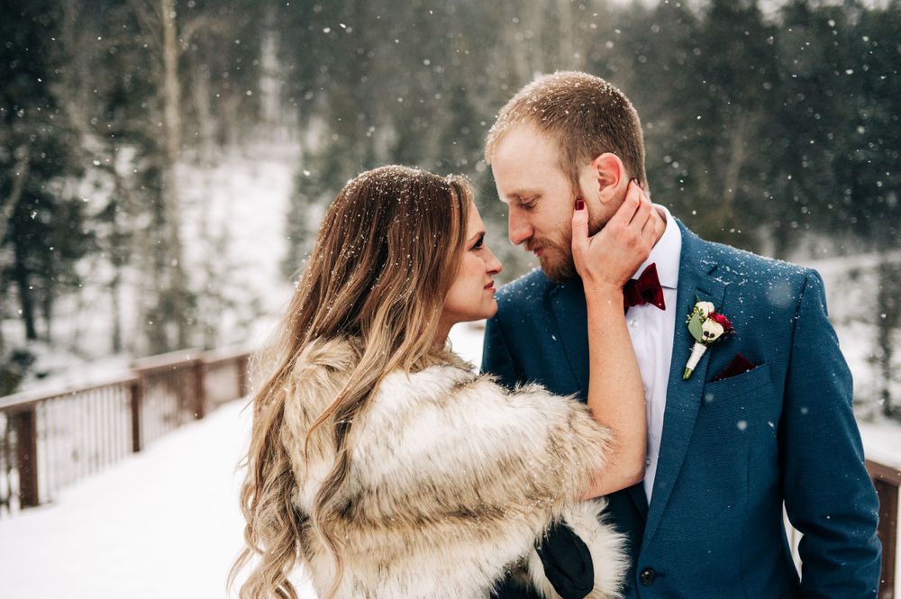 A romantic winter moment between a couple in the snow, with the bride wearing a fur wrap and groom in a navy suit.