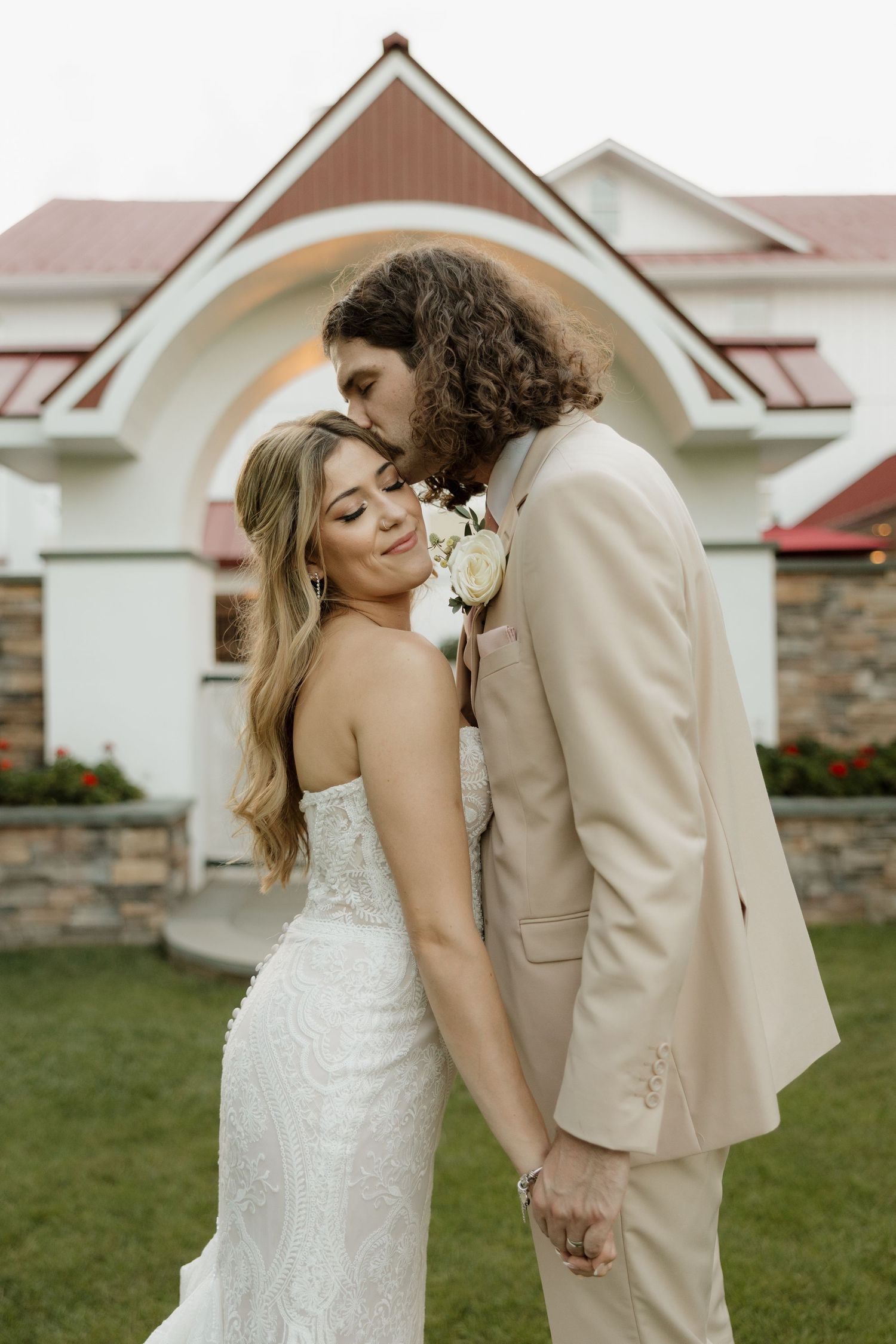 Romantic newlywed couple embracing outdoors in front of elegant white stone church with stained glass windows.