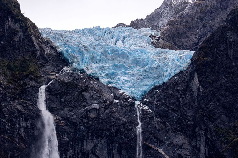 El majestuoso glaciar azul cae en cascada por la escarpada ladera de la montaña formando imponentes saltos de agua, mostrando la belleza.