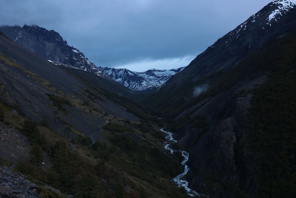Un espectacular y escarpado valle montañoso con un sinuoso río bajo un cielo crepuscular cambiante, que evoca la aventura y la exploración