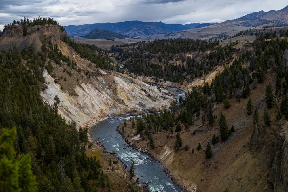 Un majestuoso río serpenteante se abre paso a través de un escarpado paisaje de cañones, con un espectacular cielo nublado sobre él.