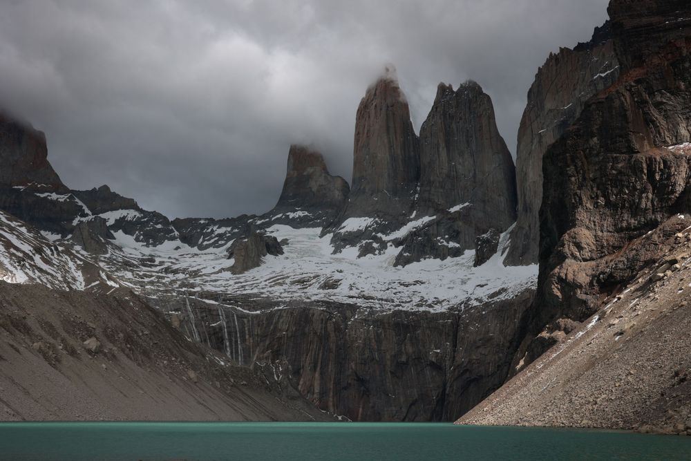 Majestuosos picos de granito atraviesan el espectacular cielo nublado sobre un sereno lago turquesa y un escarpado paisaje nevado.