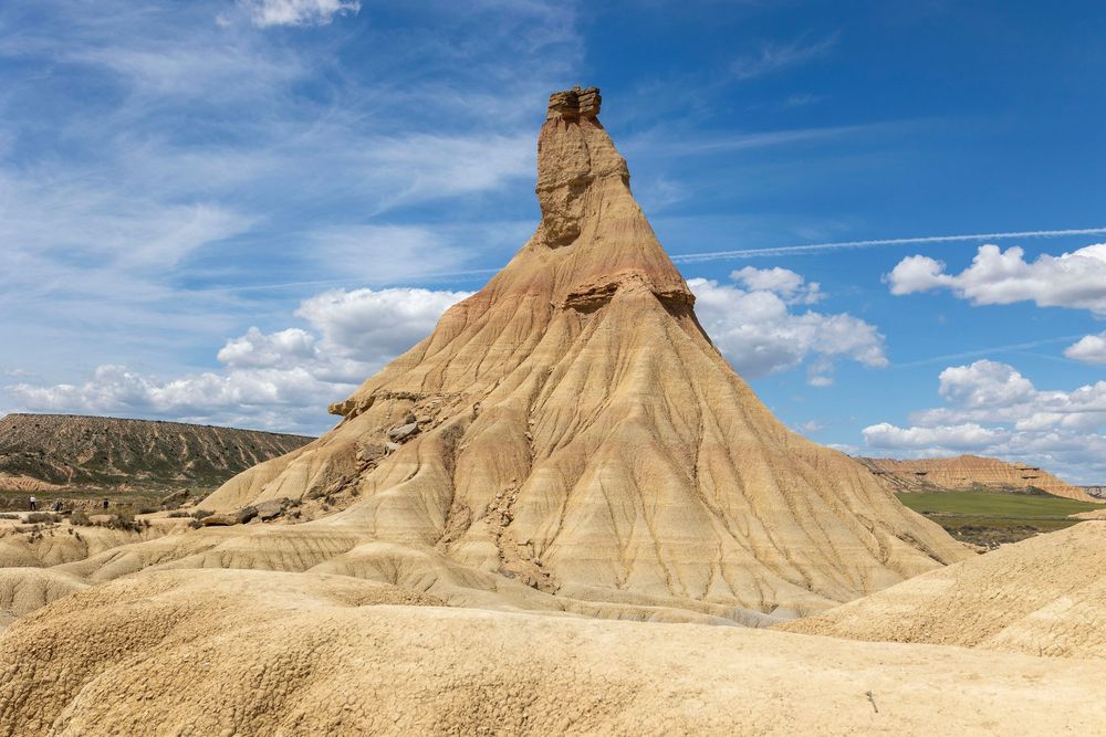 Una majestuosa formación rocosa del desierto se alza imponente bajo un cielo azul intenso salpicado de nubes, evocando la aventura