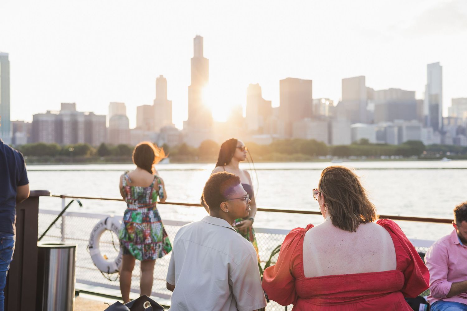 Group gathered at waterfront railing during golden hour with city skyline in background.