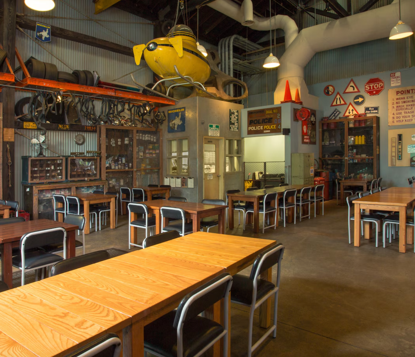 Interior of a casual restaurant dining room with wooden tables, metal chairs, and industrial-style decor.