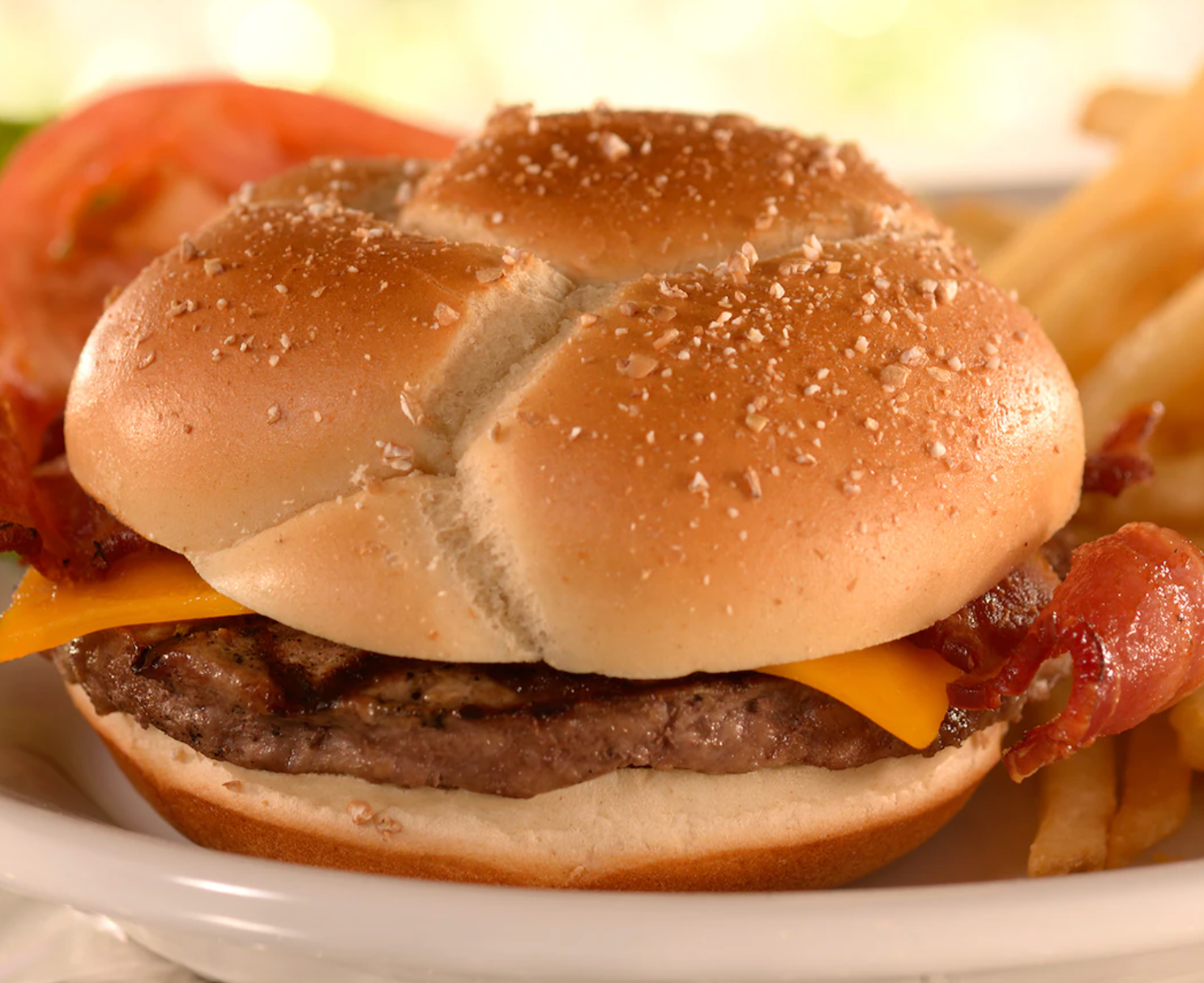 Close-up of a cheeseburger with bacon on a sesame seed bun served with french fries.