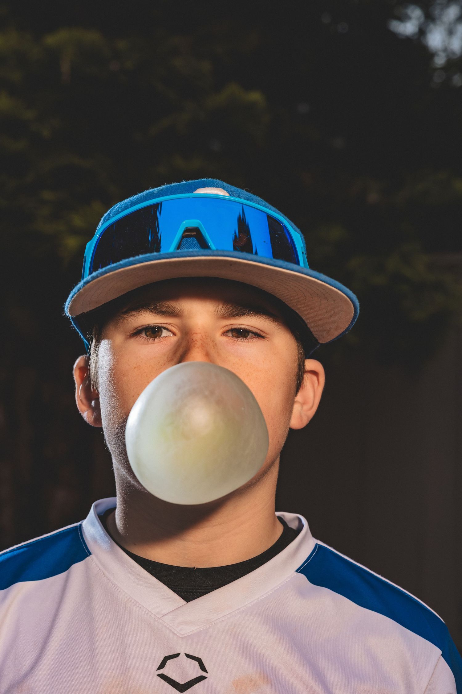 Baseball player in blue cap blowing bubble gum in dramatic outdoor portrait.