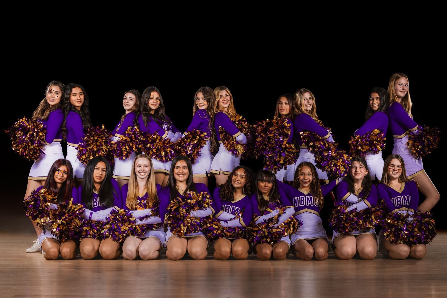 Cheerleading squad in purple and red uniforms posing for team photo on wooden floor.