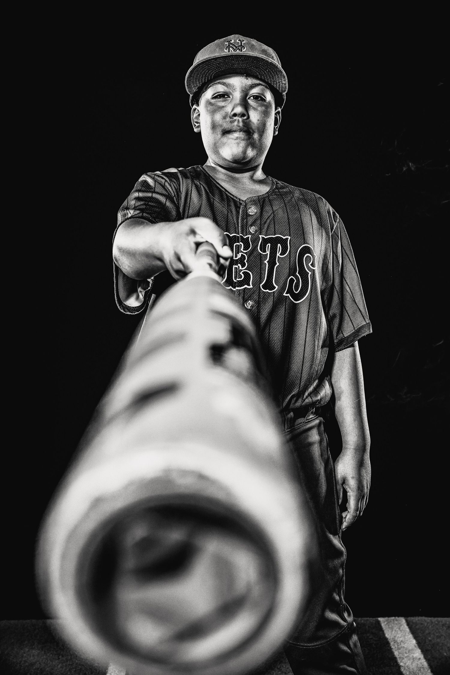 A dramatic black and white photo of a baseball player in a Mets jersey looking down at the camera through a long tube.