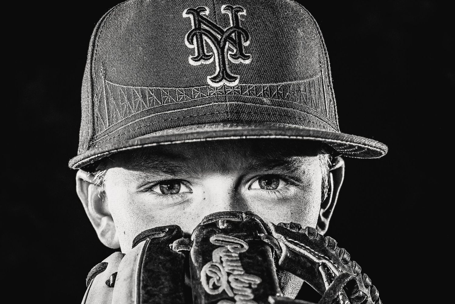 Black and white photo of a baseball player wearing a New York cap looking through their glove.