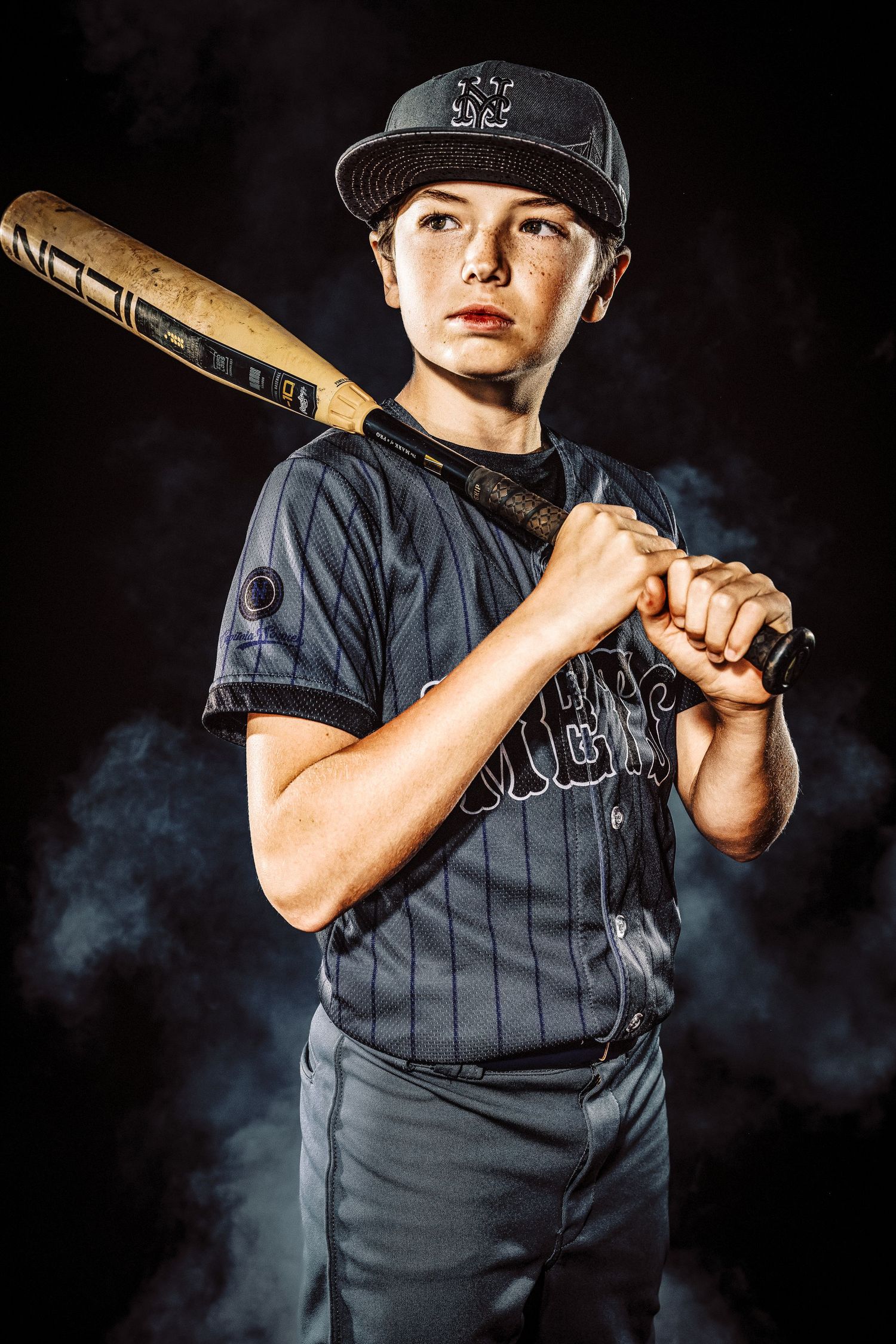Dramatic baseball photo showing player in pinstriped uniform holding wooden bat against dark smoky background.