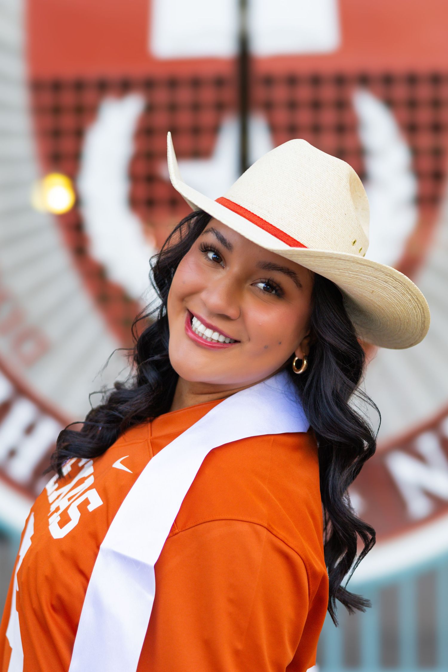 A woman in Texas Longhorns gear and cowboy hat smiles during a college sporting event.