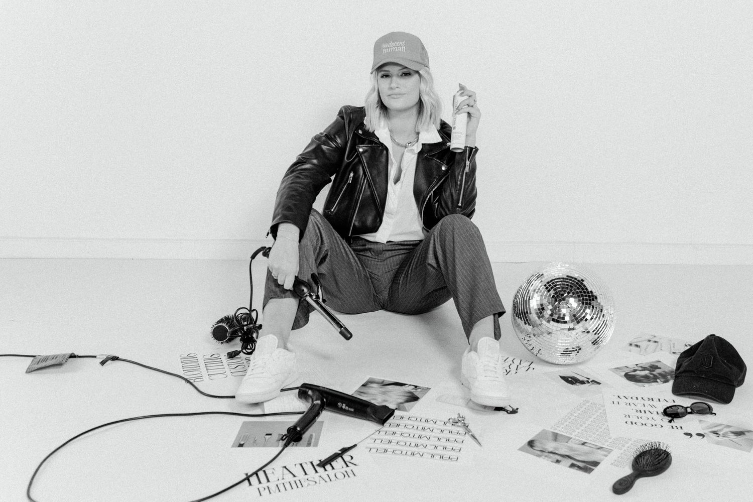 Portrait of person in leather jacket and cap sitting with disco ball and music equipment.