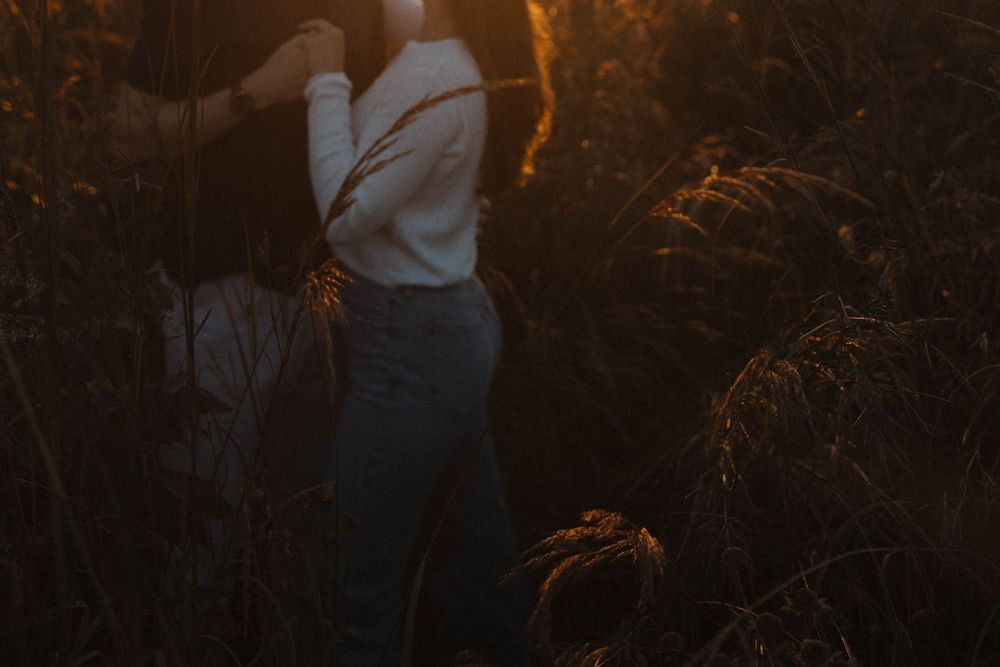 A couple shares an intimate moment in warm sunset lighting among tall grass.
