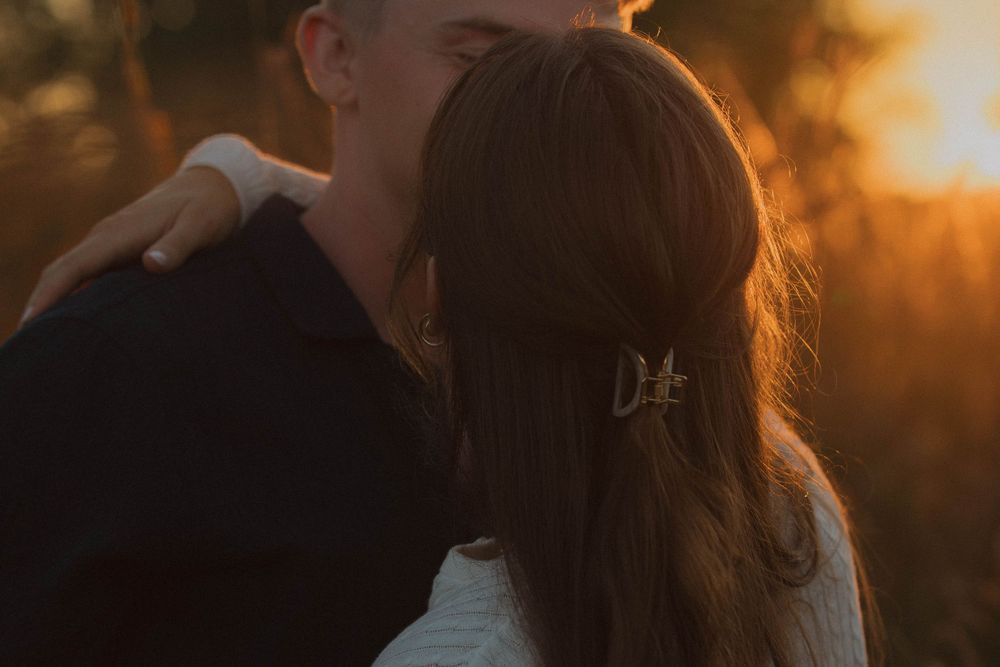 Romantic couple embraces in a golden sunset field with warm backlighting creating a dreamy atmosphere.