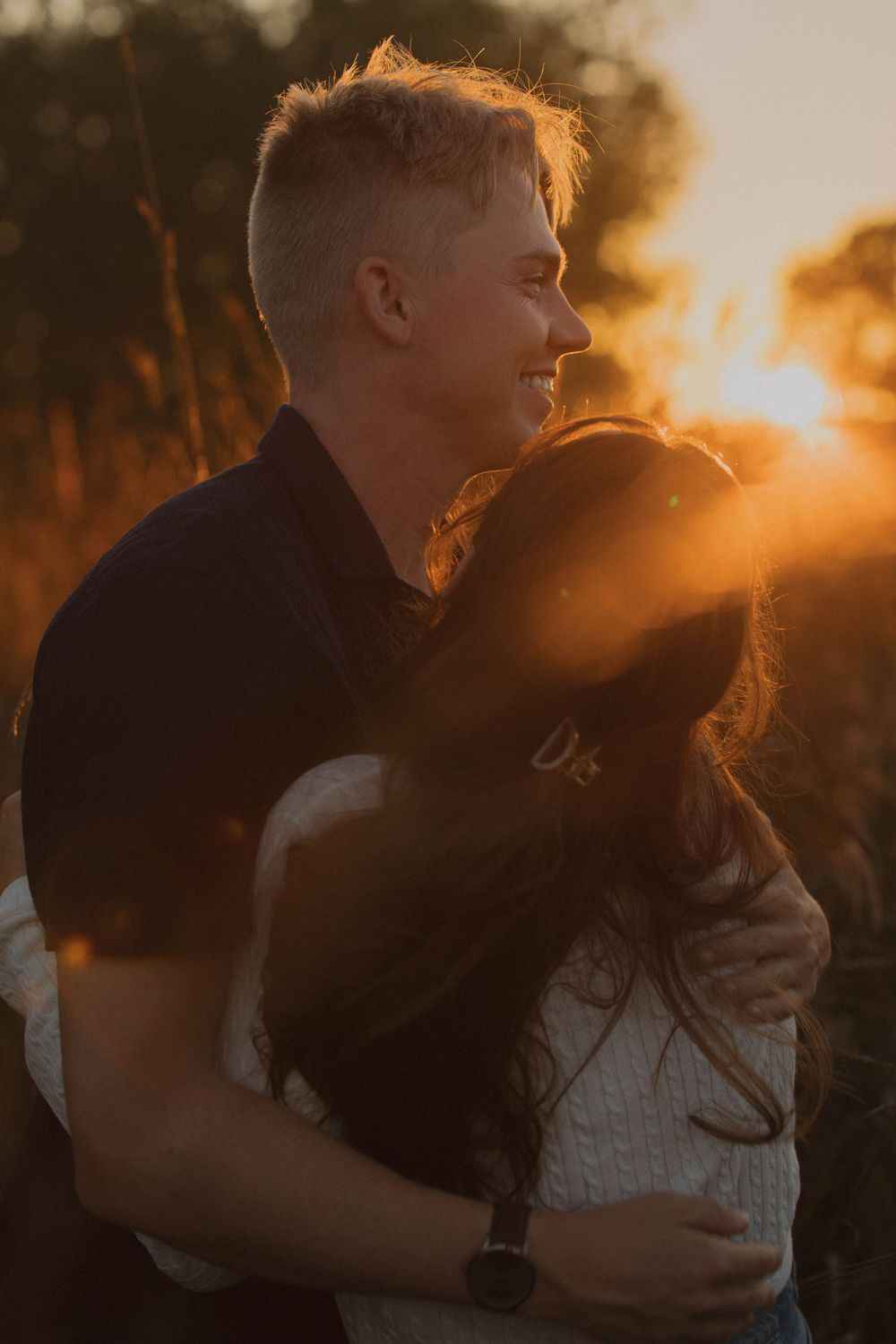 Couple shares tender moment during sunset with soft golden light filtering through trees.