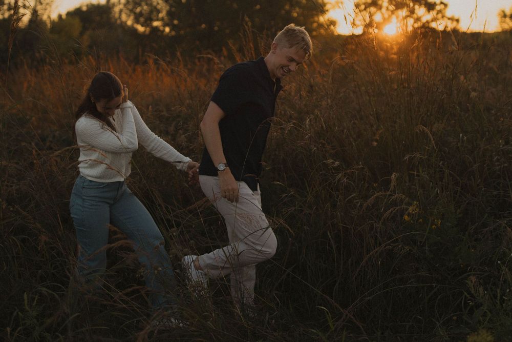 Playful couple dances and spins together in a field during golden hour.
