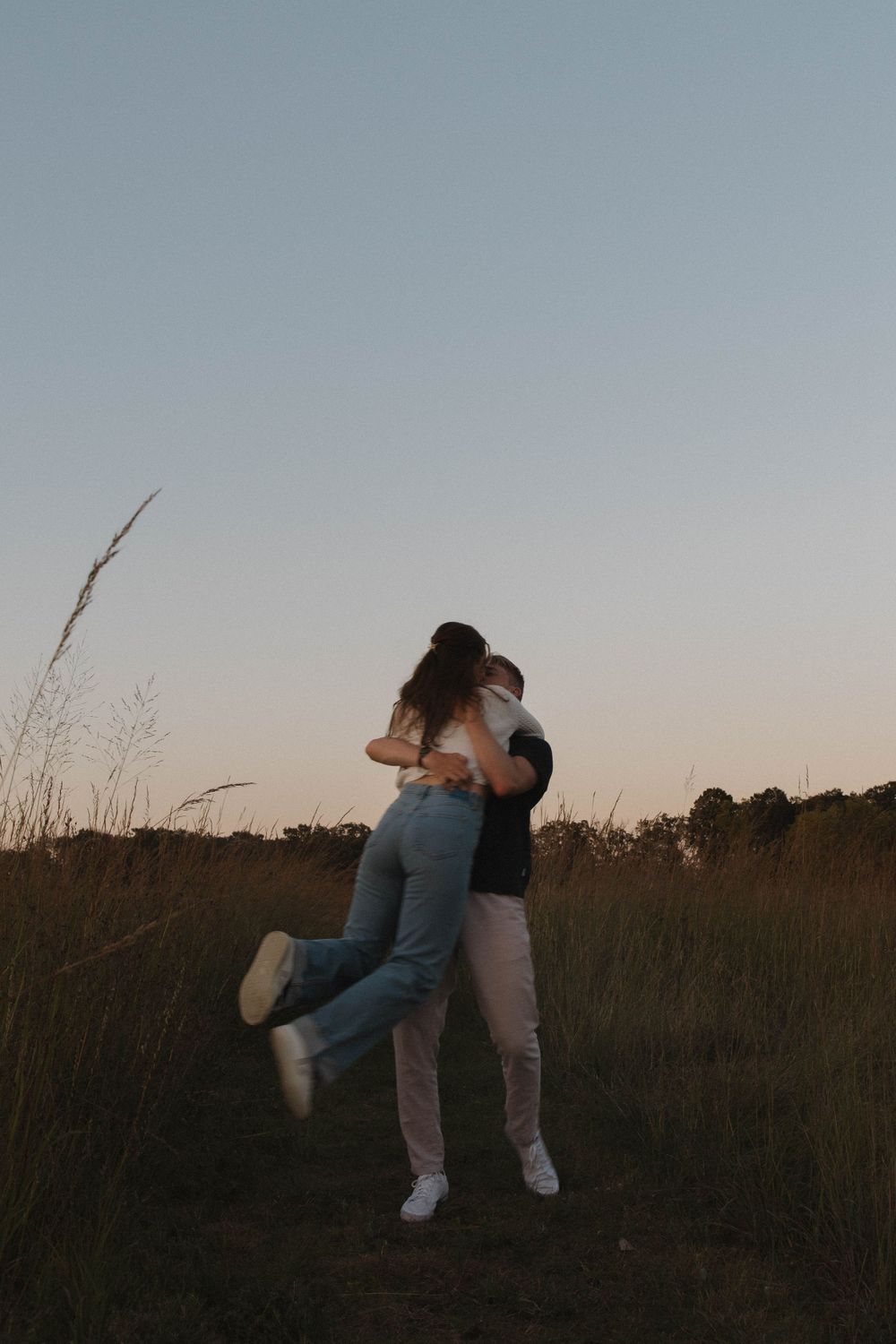 Couple dances and twirls together in a field at dusk with tall grass surrounding them.