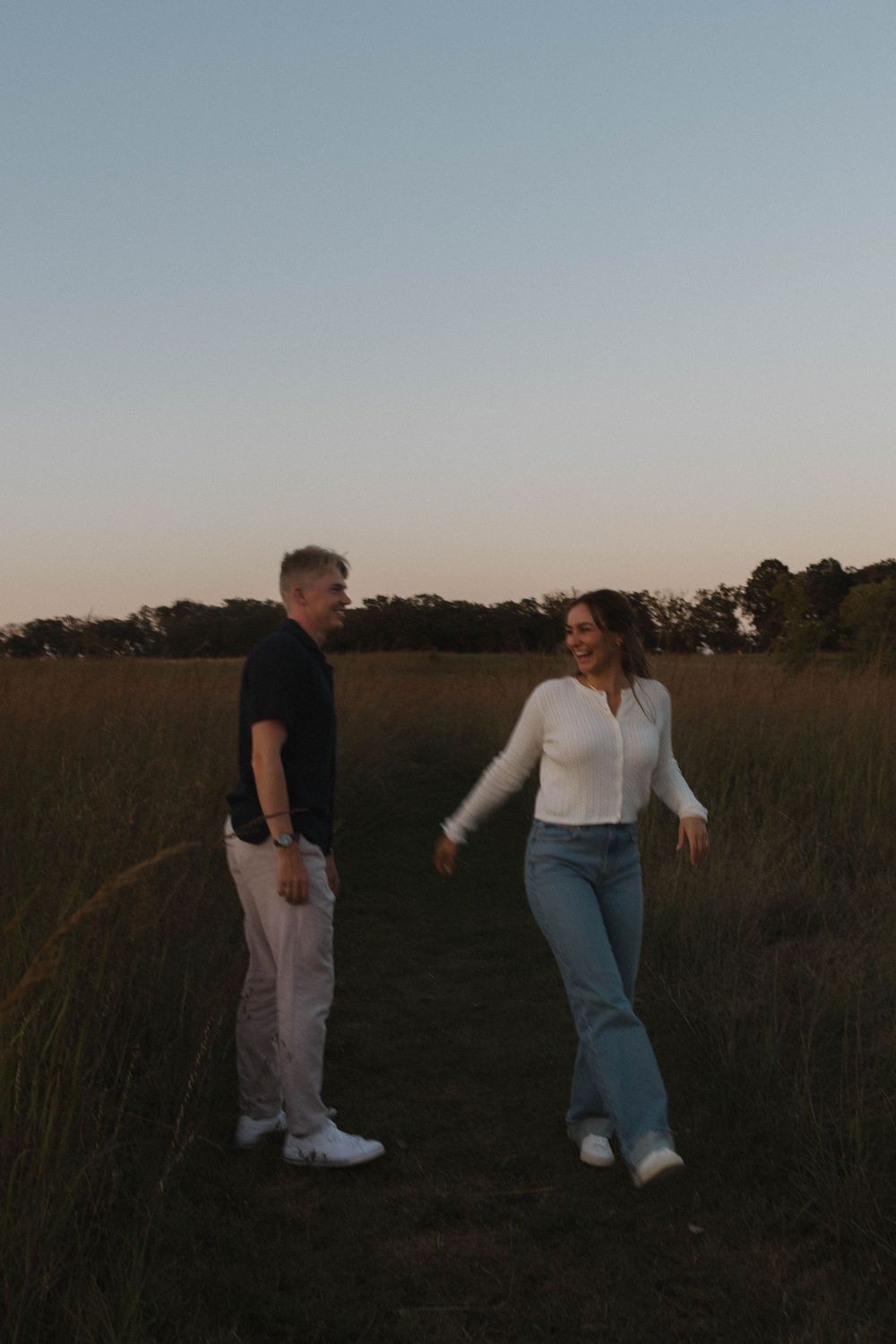 Couple enjoys a carefree moment walking through a grassy field at sunset.