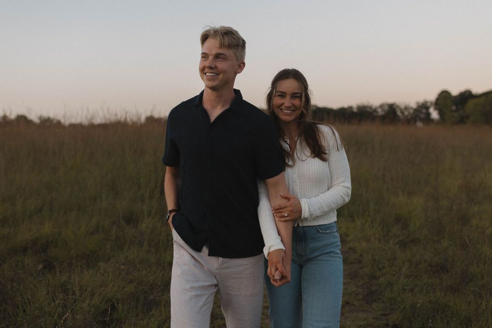 Happy couple walks arm in arm through an open field during golden hour.