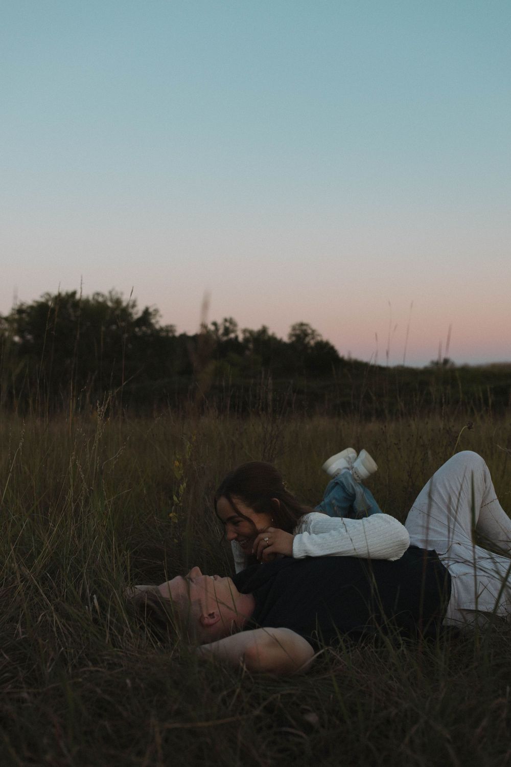 Figures resting in tall grass under a blue sky at dusk.
