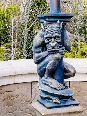 Close-up views of a decorative blue gargoyle sculpture mounted on a white stone wall in a garden setting.