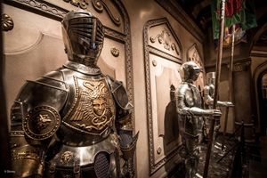 Medieval suits of armor on display in a dimly lit museum hallway with ornate gothic architectural details.