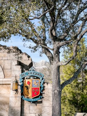 A series of rustic stone walls with ornate signs and lush green trees creating a charming entryway scene.
