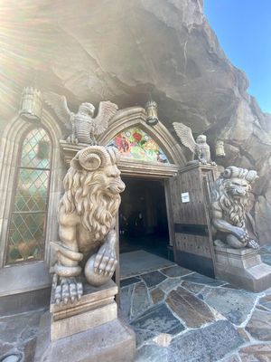 Ornate stone lion statues guard a gothic-style entrance doorway with stained glass windows carved into a rocky cave wall.