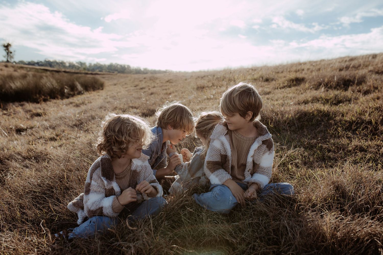 Children sitting together in a grassy meadow during sunset, sharing a heartwarming moment.