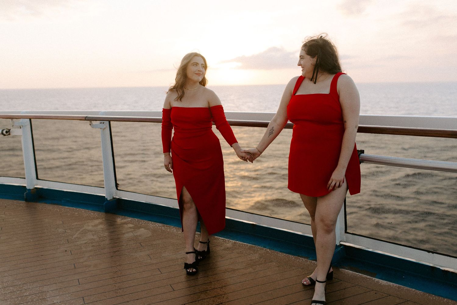 Two people in coordinated red outfits walking together on a cruise ship deck at sunset.