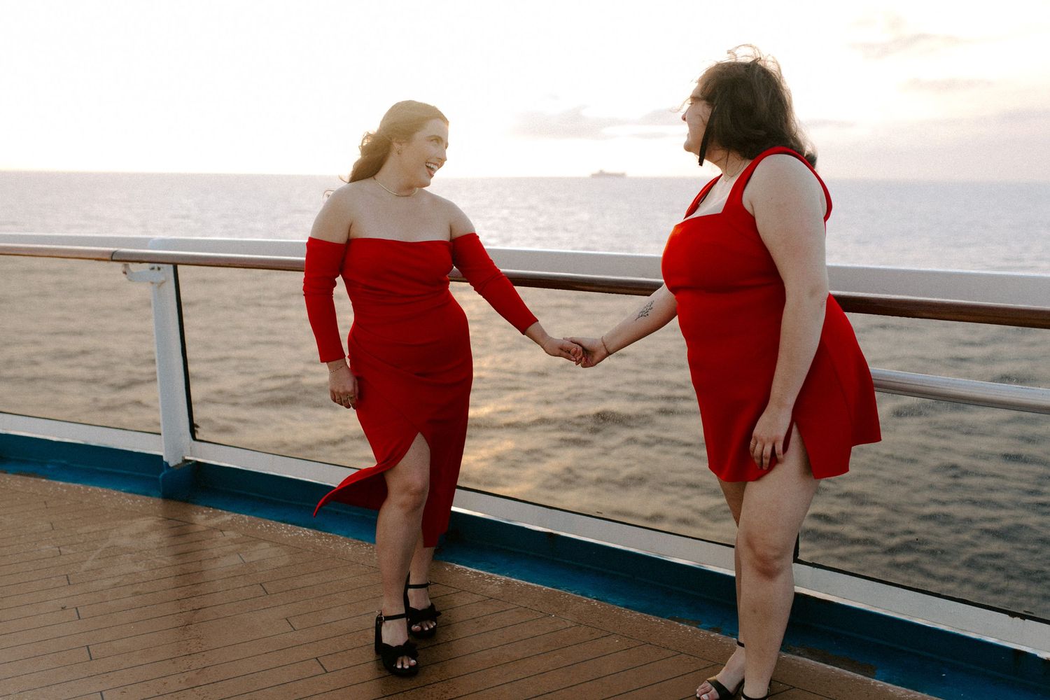 Two people holding hands while walking along a ship's railing at sunset.